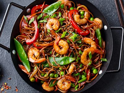 Stir fry noodles with vegetables and shrimps in black iron pan. Slate background. Top view.